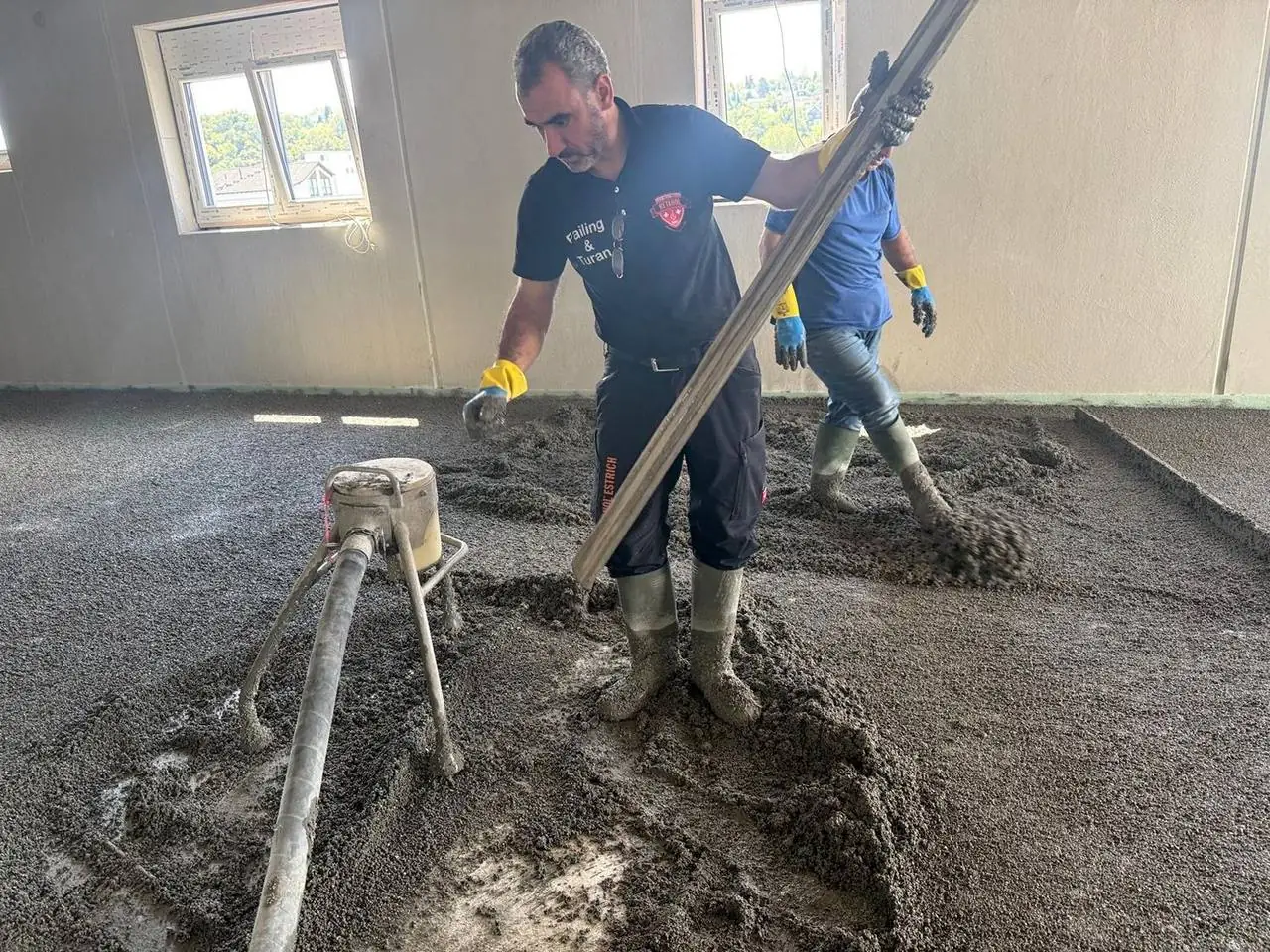Mitarbeiter bringt Estrich mit dem Schlauch ein
