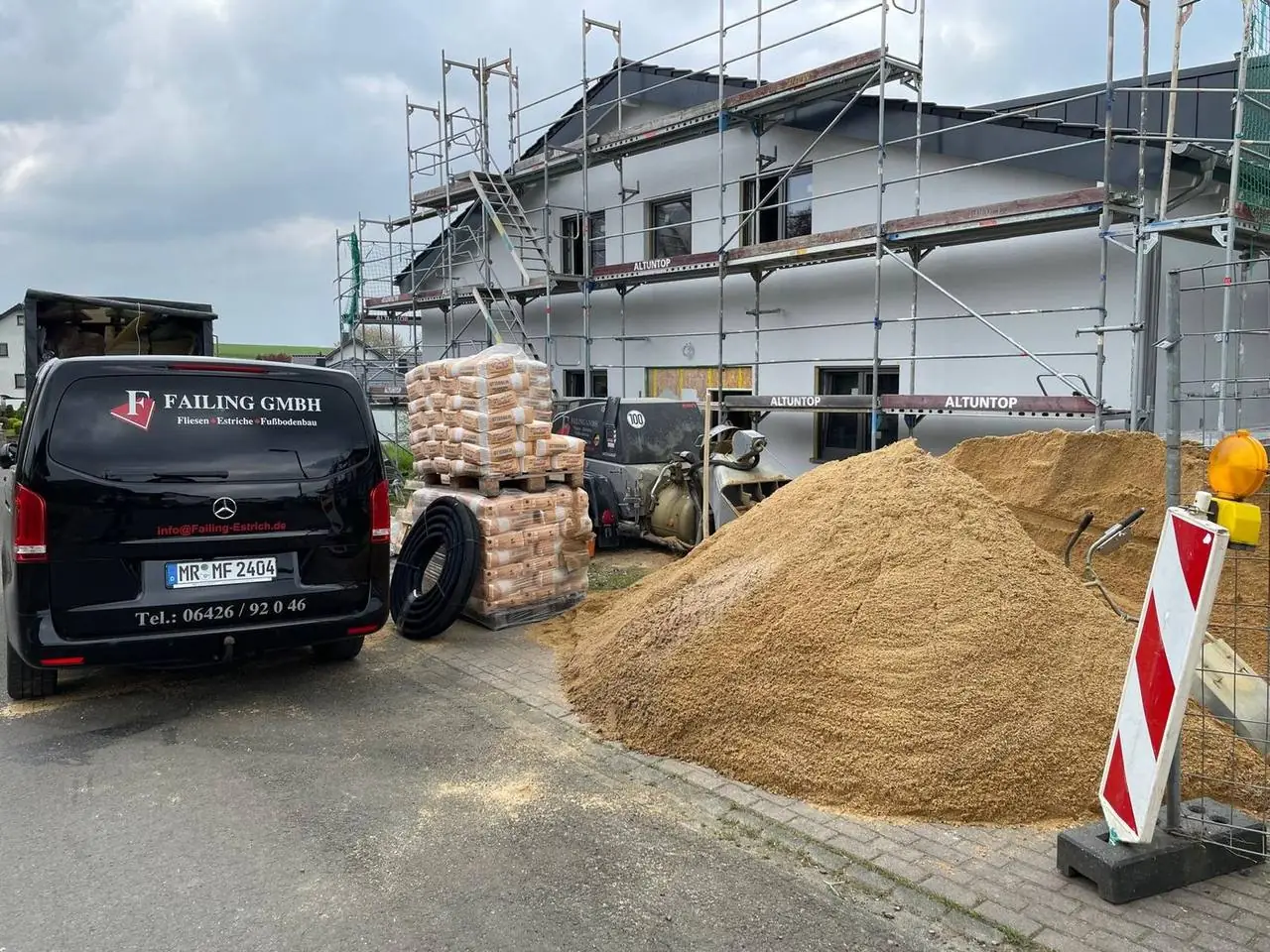 Sand, Zement und Firmenfahrzeug vor einem eingerüsteten Neubau